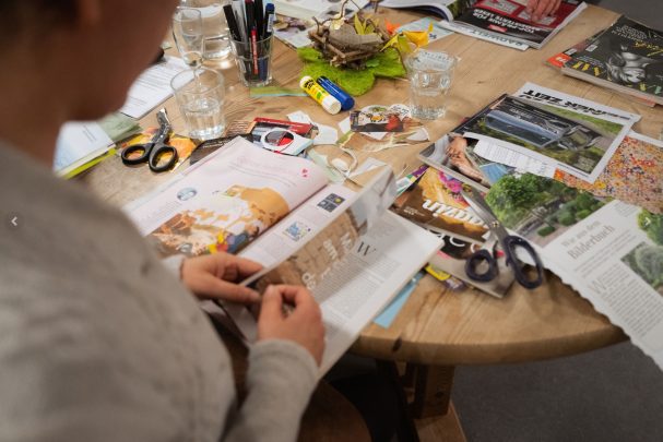 Person schneidet Bilder aus Zeitschriften auf einem Tisch mit Bastelmaterialien.